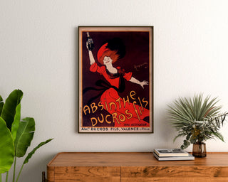 Vintage reclameposter Absinthe Ducros, ingelijst boven een houten dressoir, tussen planten.