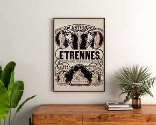 Vintage reclameposter Verdun, beeldjes en geschenken, ingelijst boven een houten ladekast, tussen planten.