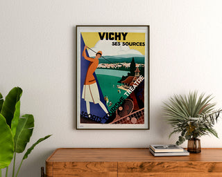 Vintage toeristische poster – Vichy, bronnen en toerisme, ingelijst boven een houten dressoir, tussen planten.