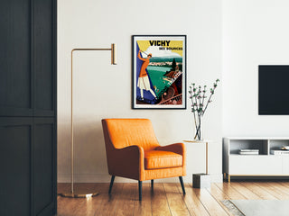 Vintage toeristische poster – Vichy, bronnen en toerisme, ingelijst in een woonkamer met een oranje fauteuil en een vloerlamp.