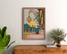 Vintage wijnposter – Au bon vin d’Alsace – Hansi, ingelijst boven een houten dressoir tussen planten.