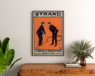 Vintageposter A Brace of Partridges, Strand Theatre, ingelijst boven een houten dressoir, tussen planten.