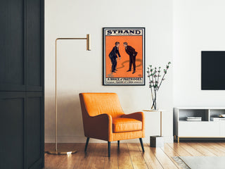 Vintageposter A Brace of Partridges, Strand Theatre, ingelijst in een woonkamer met een oranje fauteuil en een vloerlamp.