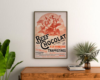 Vintage poster Beef Chocolat, chocolaterie de la Drôme, ingelijst boven een houten ladekast, tussen planten.