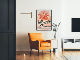 Vintage poster Beef Chocolat, chocolaterie de la Drôme, ingelijst in een woonkamer met een oranje fauteuil en een staande lamp.