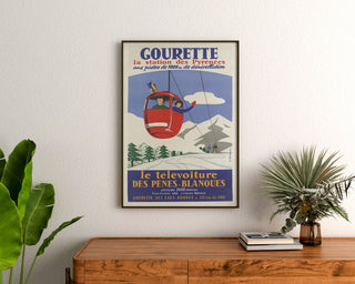 Vintageposter Gourette, télévoiture, ingelijst boven een houten ladekast tussen planten.