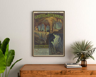 Vintageposter Grottes de Bétharram, ingelijst boven een houten ladekast tussen planten.