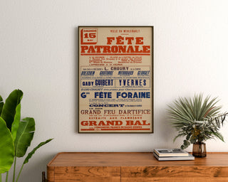 Vintage poster Le Merlerault, dorpsfeest, ingelijst boven een houten dressoir, tussen planten.