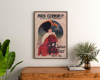 Vintage poster Paris-Clermont, winters seizoen, ingelijst boven een houten dressoir, tussen planten.