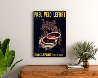 Vintage poster Fietsbanden Lefort, ingelijst boven een houten ladekast, tussen planten.