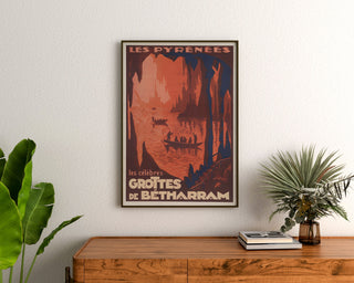 Vintageposter Pyrénées, grottes de Bétharram, ingelijst boven een houten ladekast tussen planten.