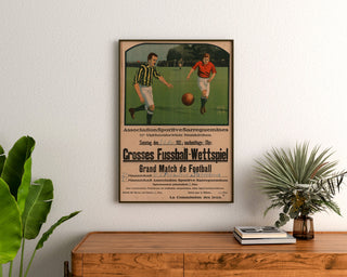 Vintage poster Sarreguemines, voetbalwedstrijd, ingelijst boven een houten ladekast, tussen planten.