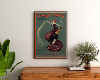 Vintageposter Woman and Wine, Princess’s Theatre, ingelijst boven een houten dressoir, tussen planten.